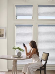 Woman sitting at a table in the dining room that has a window with Sonnette Cellular Roller Shades installed