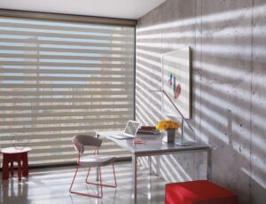 Office desk with a computer beside a window with Designer Banded Shades installed