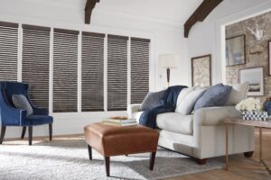 Living room with a couch and chair in front of windows with Parkland Wood Blinds installed