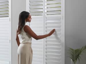 Lady in a living room touching her newly installed NewStyle Hybrid Shutters