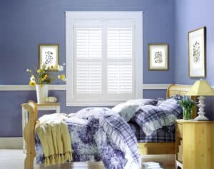 Blue bedroom with bed with Palm Beach Polysatin Shutters on the window