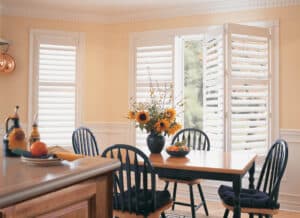 Dining room with dark table in front of windows adorned with Palm Beach Polysatin Shutters