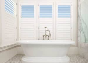 Bathroom with white tub infrom of Palm Beach Polysatin Shuttered windows