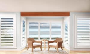 Living room with two chairs in front of big windows with Palm Beach Polysatin Shutters