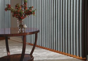Close up of Cadence Soft Vertical Blinds installed on a window near a table with a vase
