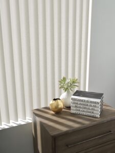Close up of a window above a corner night stand with Cadence Soft Vertical Blinds installed