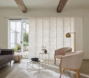 Two chairs with tables in a living room where the windows are covered with Skyline Gliding Window Panels