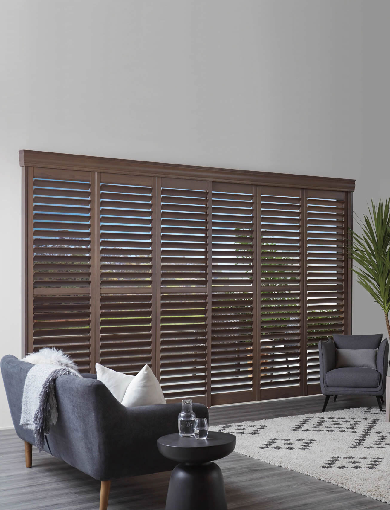 Window covered with brown Hunter Douglas shutters, and a chair in the foreground.