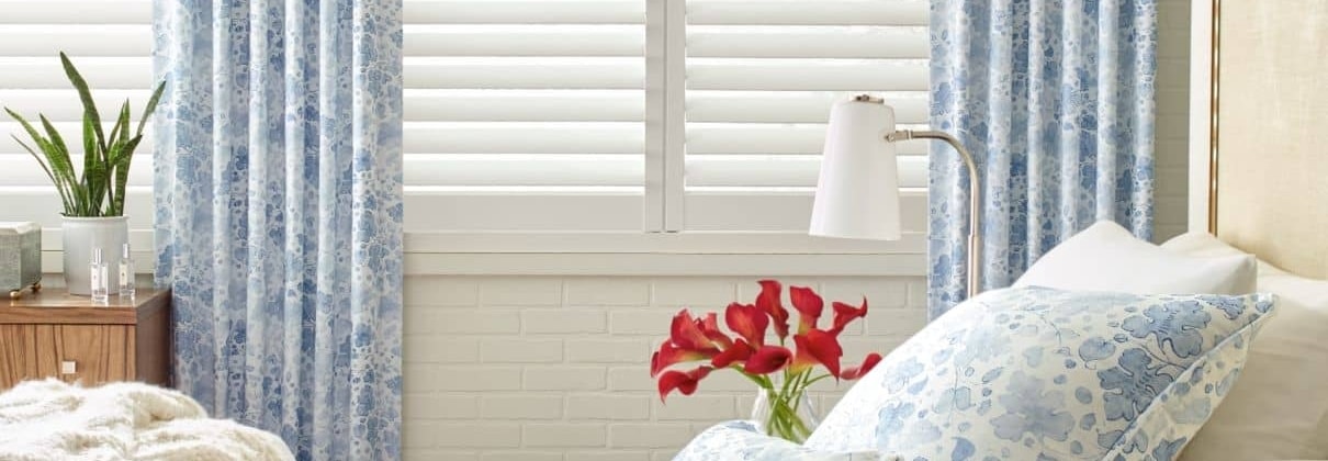 A bedroom with blue and white curtains, providing window covering inspiration for a cozy bed.