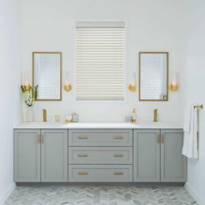 A bathroom with a gray vanity, gold mirrors, and Venetian blinds.