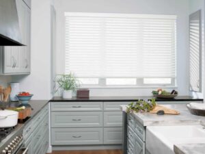 A kitchen with gray cabinets and white counter tops featuring venetian blinds.