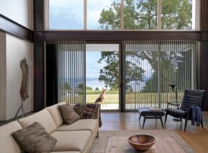 A living room with large windows featuring sheer shades overlooking a lake.