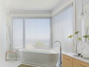 A bathroom with sheer shades and a view of the city.