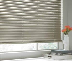 A window with venetian blinds and a vase of flowers.