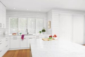 A white kitchen with a marble counter top adorned with sheer shades.