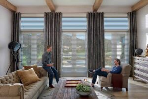 Two men sitting in a living room with sheer shades.