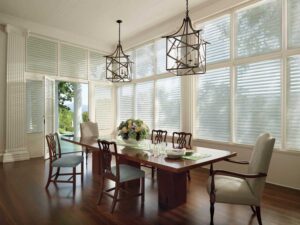 A dining room with large windows filtered using sheer shades, providing privacy and natural light ambiance. The room is adorned with a table, creating a delightful space for meals and gatherings.